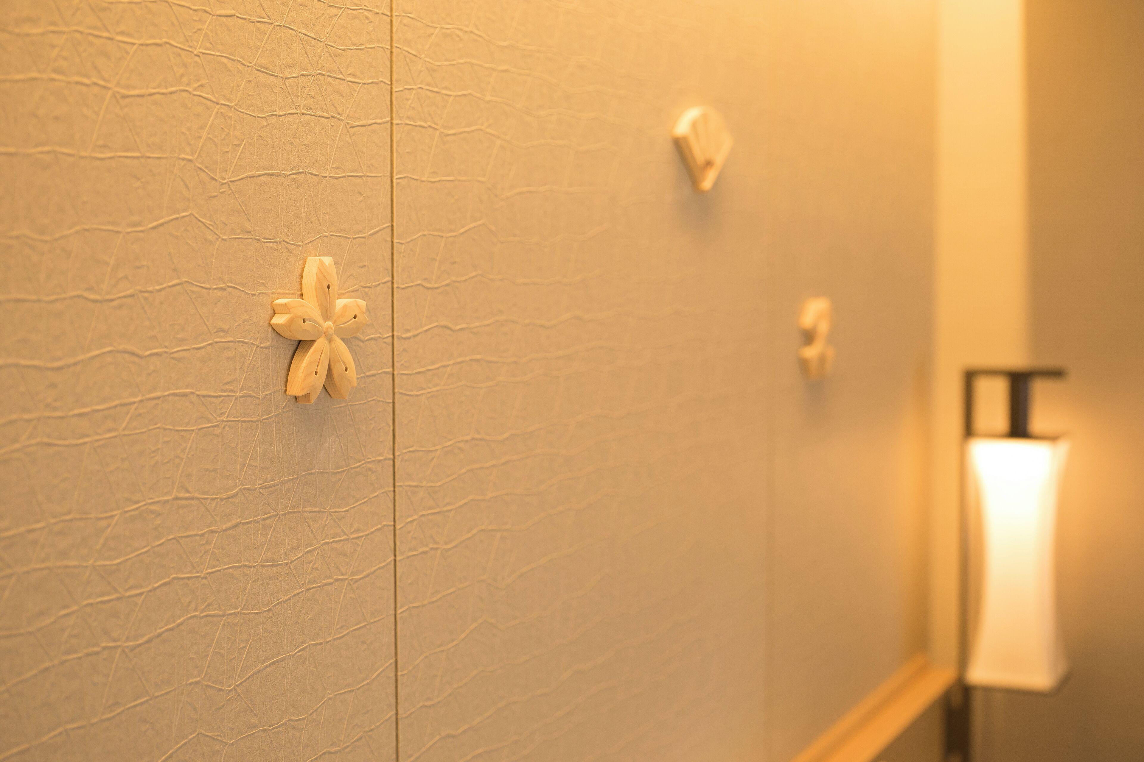 A textured wall with a wooden flower-shaped decoration and a wall-mounted light fixture.