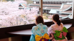 Two individuals in traditional attire sitting by a window overlooking a building with traditional architecture and cherry blossoms. - Kotohira Grand Hotel Sakuranosho (Kotohira)