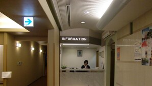 A reception area with a receptionist, a sign for the information desk, and a waiting bench.