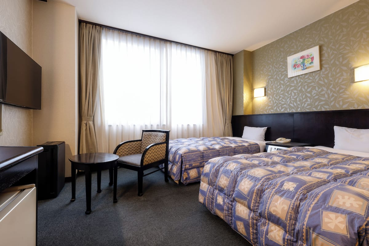 A hotel room with two beds, a desk, a chair, and a television.