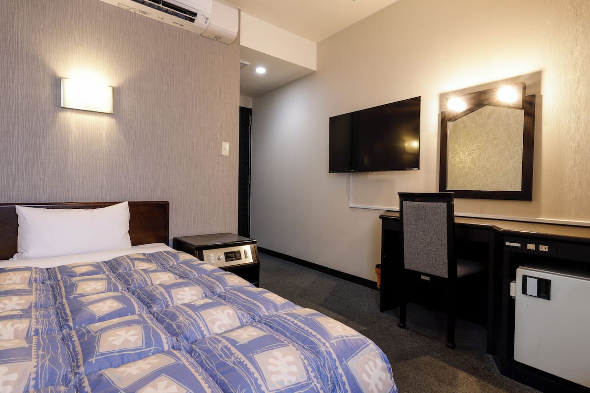 A hotel room with a bed, a desk, a chair, a television, and a small refrigerator.