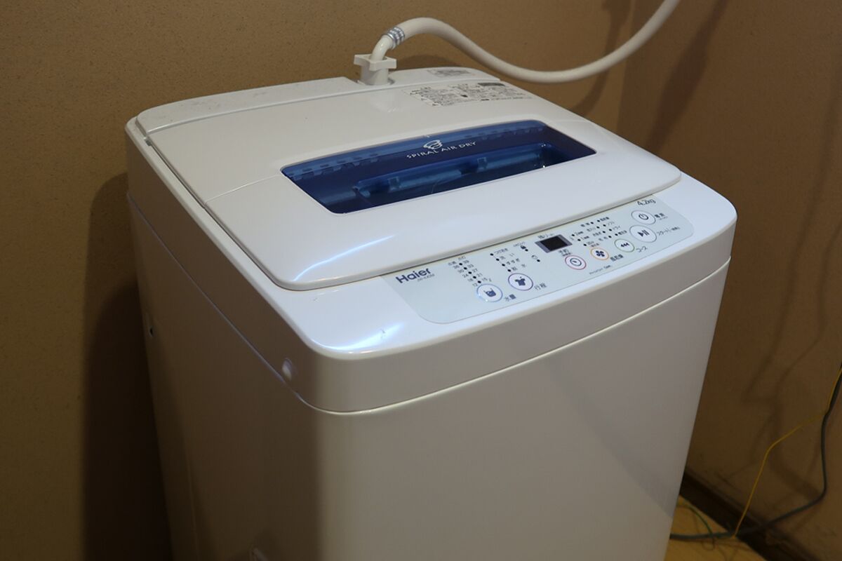 Un electrodoméstico blanco, compacto y de diseño moderno, con pantalla digital y panel de control, probablemente una lavadora o secadora, frente a una pared lisa.