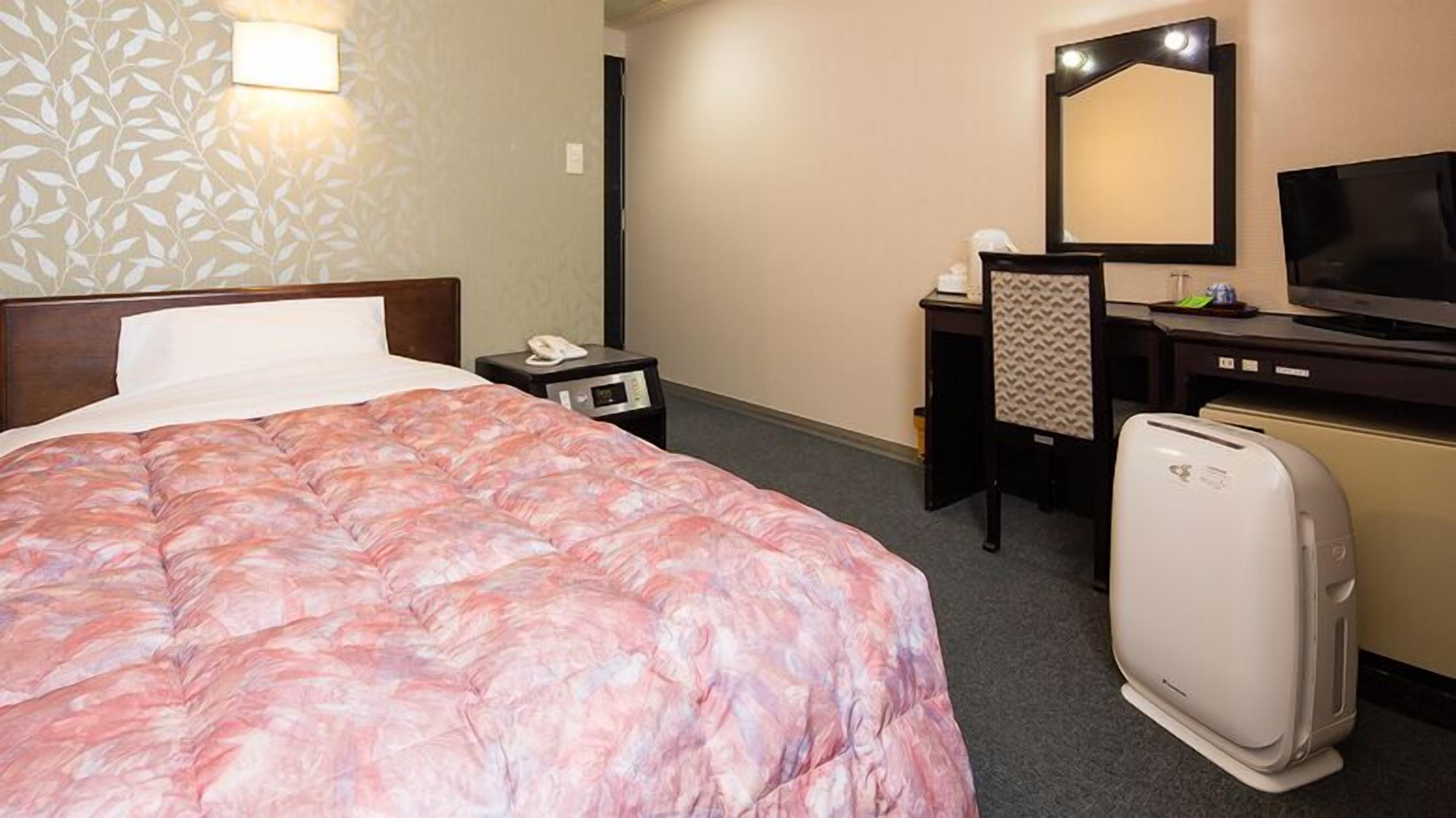 A hotel room with a bed, a desk, a mirror, a television, and a refrigerator.