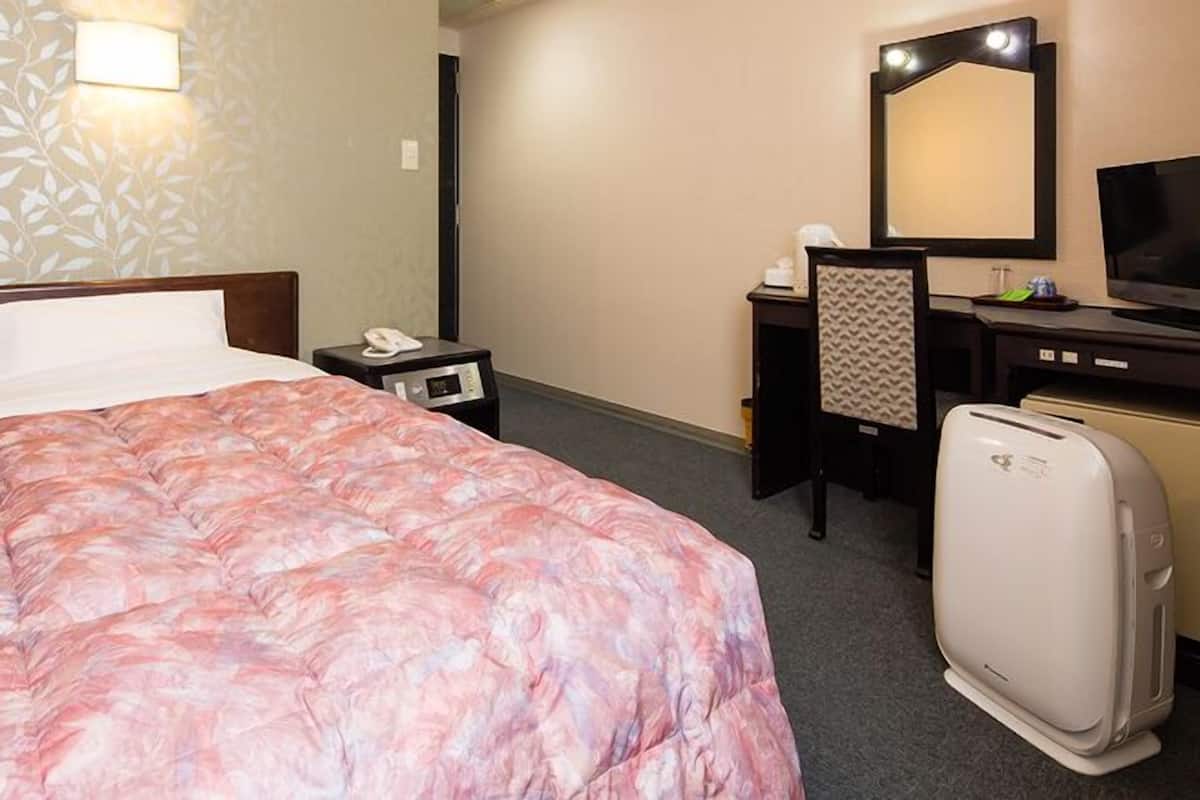 A hotel room with a bed, a desk, a mirror, a television, and a refrigerator.