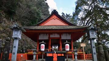 A traditional Japanese shrine with a red roof and white walls, surrounded by trees.