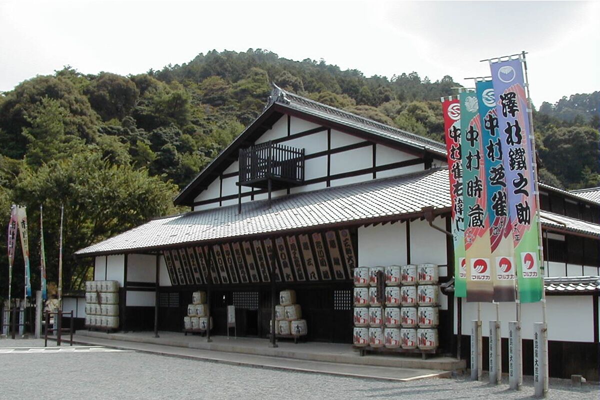 A traditional Japanese building with a tiled roof and wooden beams, surrounded by lush greenery.
