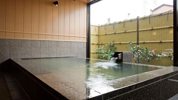 A hot spring bath with a view of a bamboo fence and greenery outside.
