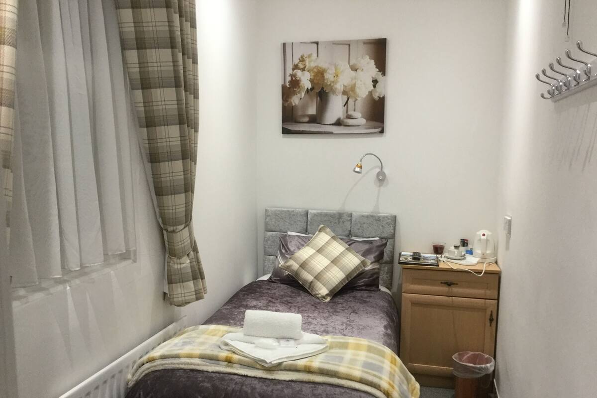 A small, neatly arranged bedroom with a bed, a bedside table, a lamp, and a wall-mounted picture.