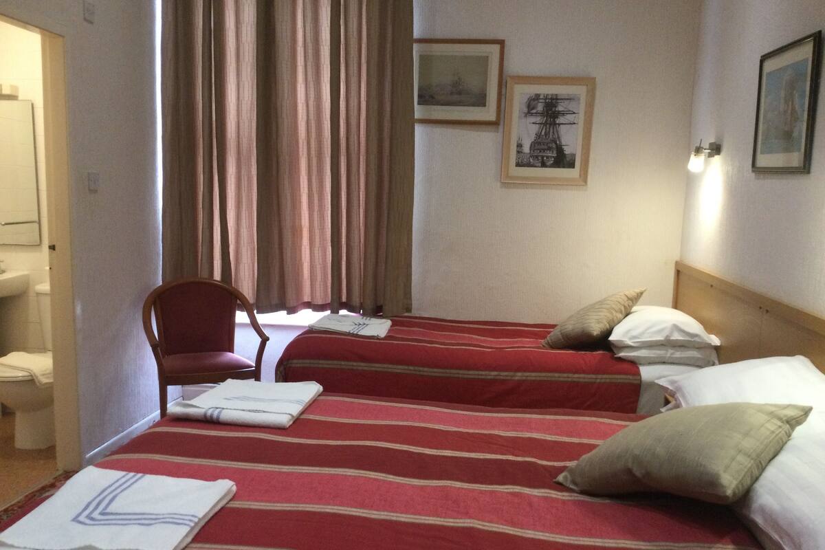 A hotel room with two beds, a chair, a sink, and two framed pictures on the wall.