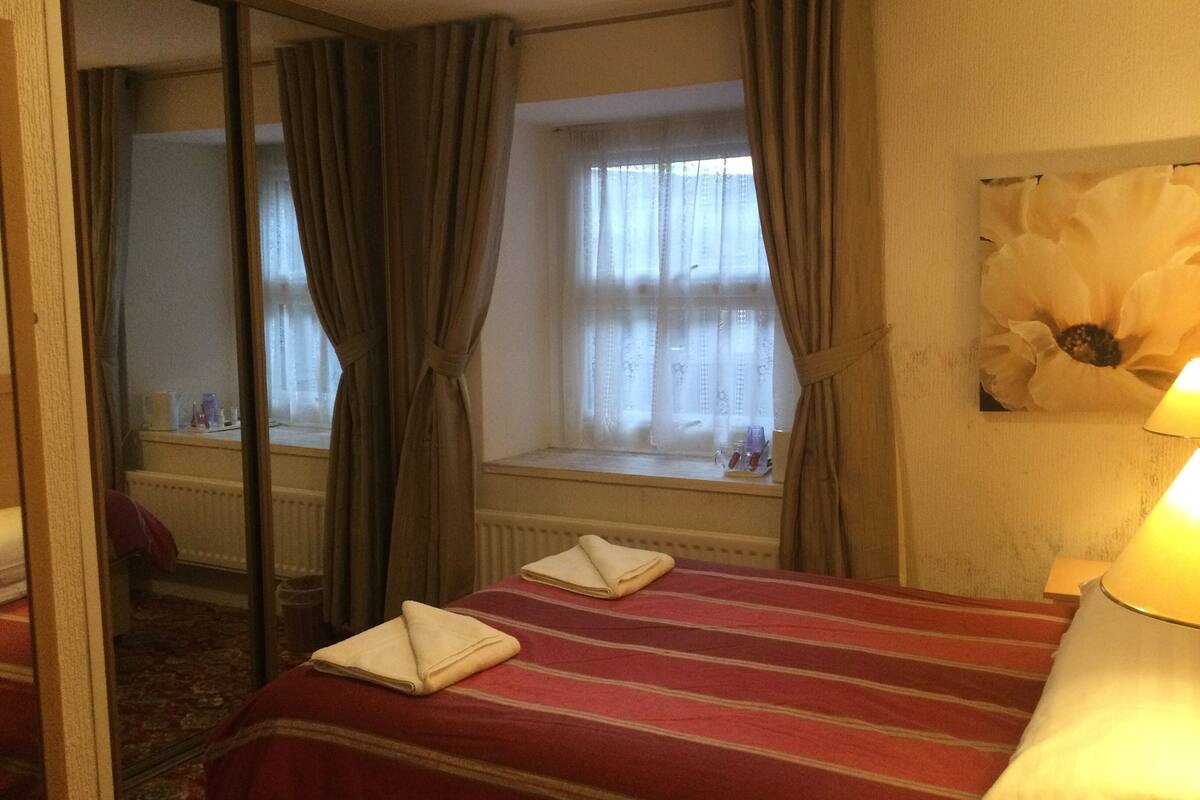 A hotel room with a bed, a window with curtains, a radiator, and a lamp.