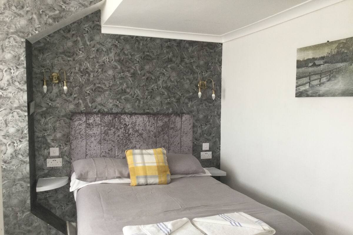 A bedroom with a grey bed, a yellow and grey pillow, and a painting on the wall.