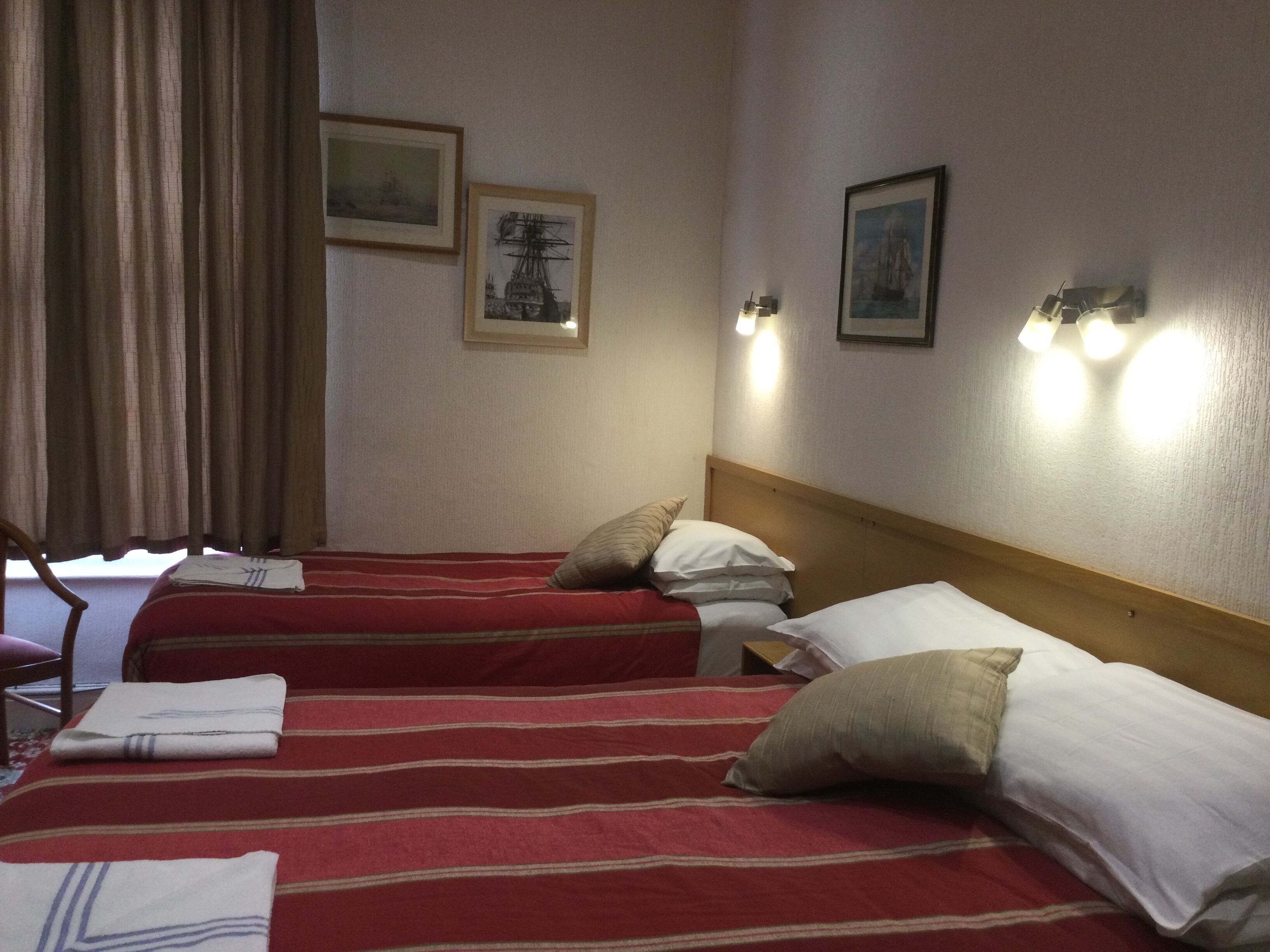Een hotelkamer met twee bedden, elk voorzien van rode en witte beddengoed, een houten hoofdbord en wandlampen.