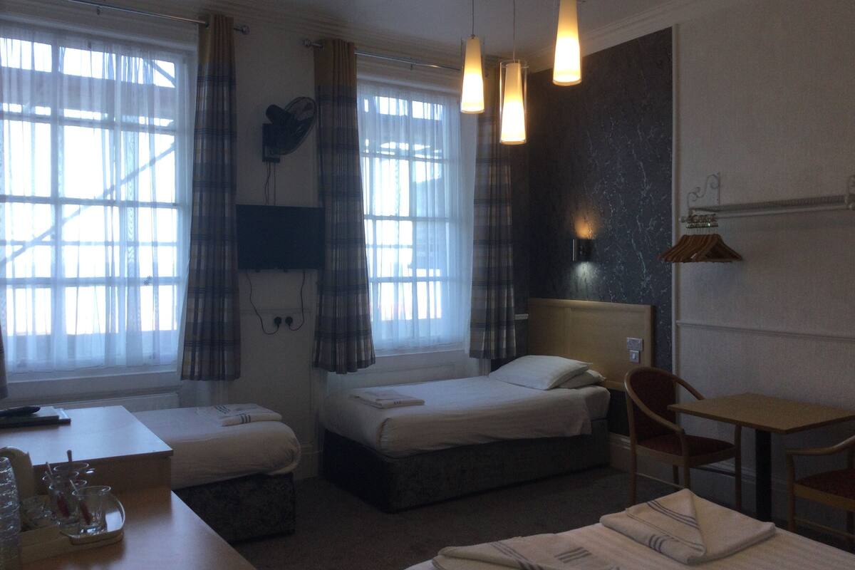 A hotel room with two beds, a desk, a chair, a TV mounted on the wall, and a window with curtains.