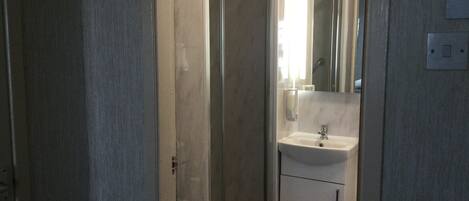 A bathroom with a glass shower door, a sink with a mirror, and a light switch on the wall.