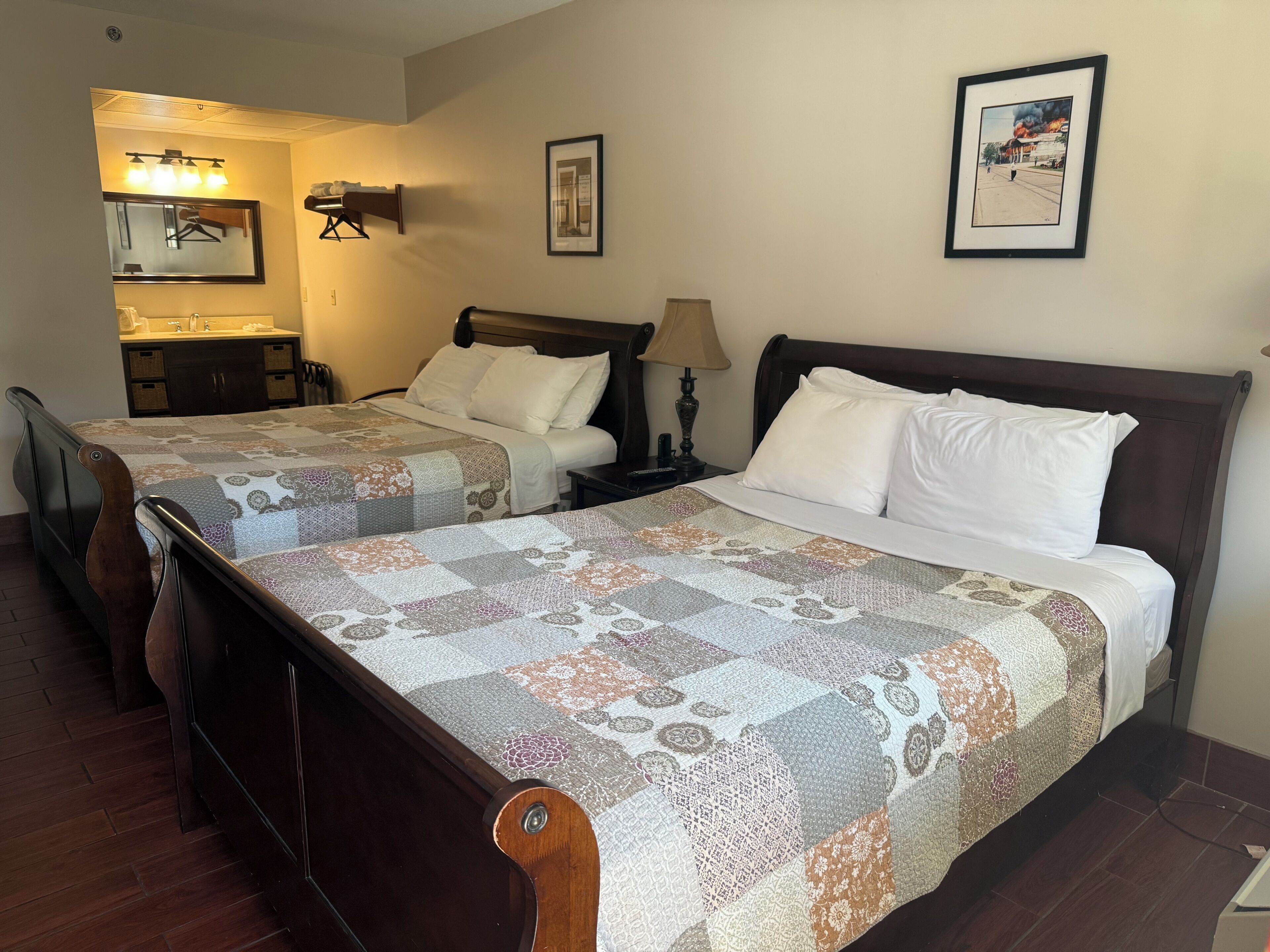 A hotel room with two beds, a bathroom, a mirror, and a framed picture on the wall.