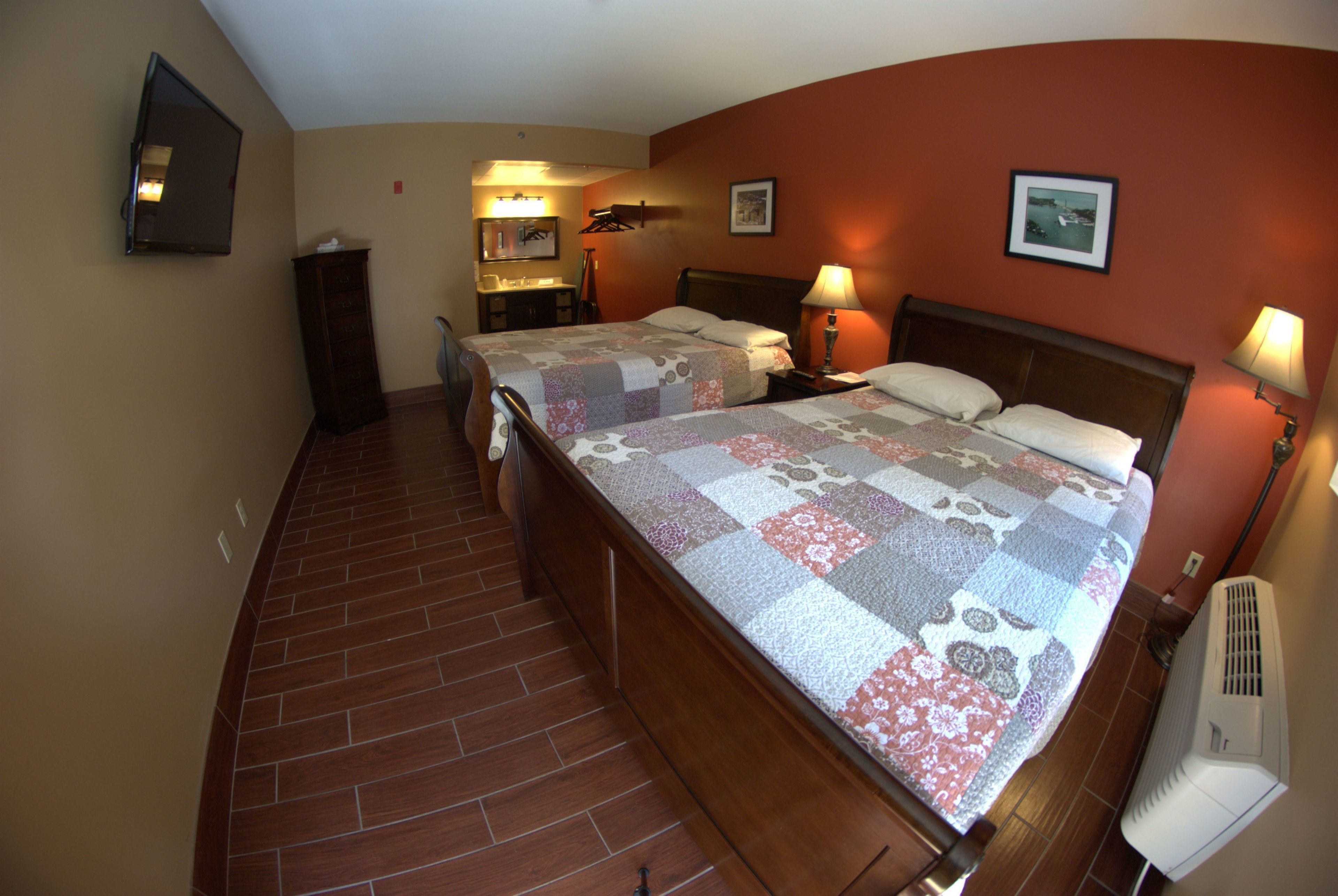 A hotel room with two beds, a desk, a chair, a wardrobe, and a wall-mounted TV.