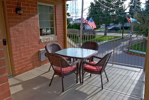 Une terrasse avec une table en verre et des chaises en osier, un mur de briques et une vue sur la rue, où flottent des drapeaux américains.