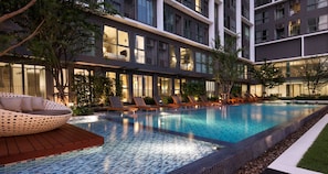 A modern hotel with a swimming pool, lounge chairs, and a well-lit interior.
