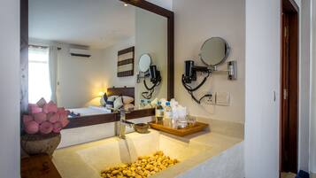 A bathroom with a large mirror, a sink with a tray of toiletries, and a bowl of yellow pebbles.