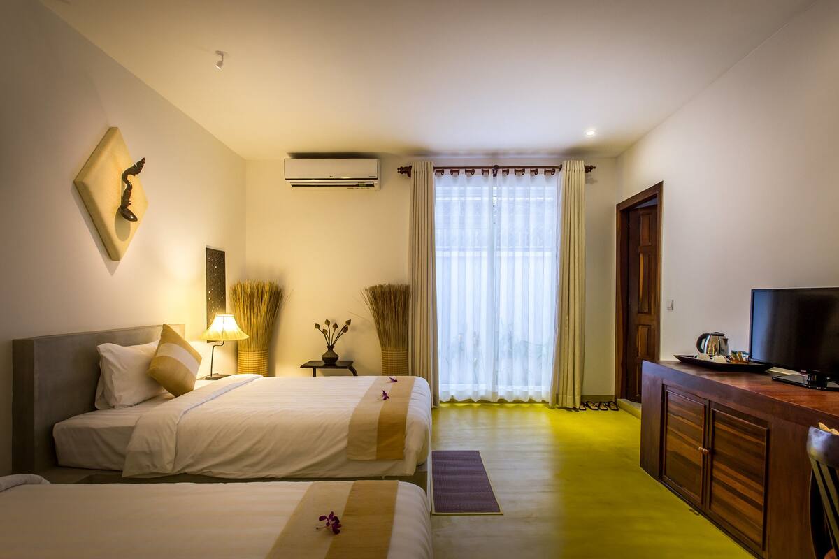 A hotel room with two beds, a TV, a desk, and a large window with curtains.