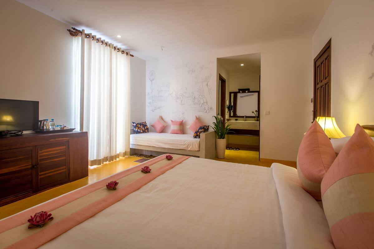 A hotel bedroom with a bed, a TV, a desk, and a bathroom visible through an open door.