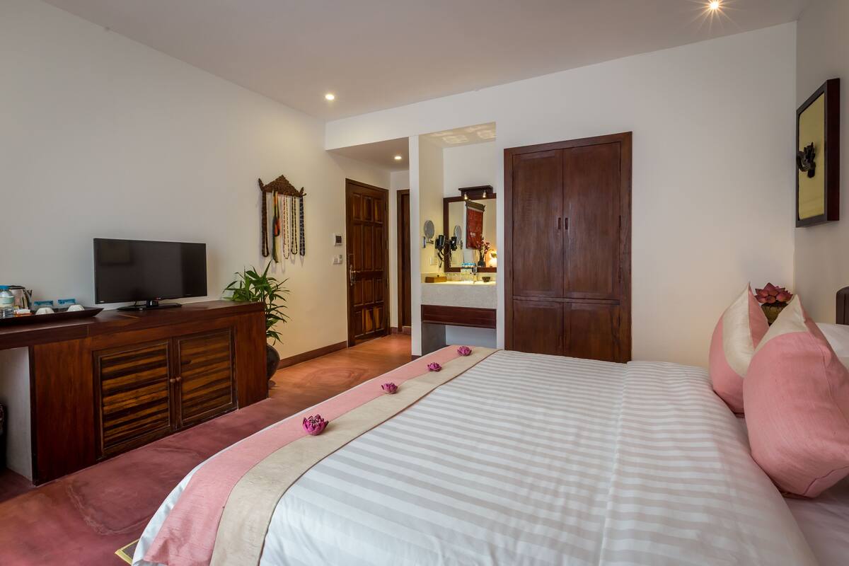 A hotel room with a bed, a TV, a desk, and a bathroom visible through an open door.