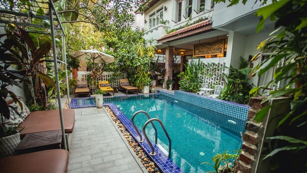 A swimming pool with a blue tiled edge, surrounded by lounge chairs and potted plants. - VMANSION Boutique Hotel (Phnom Penh)