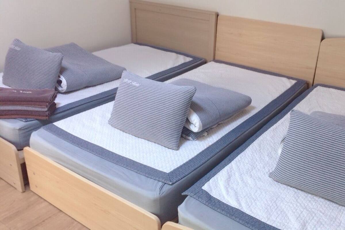 A set of three neatly made beds with striped bedding and pillows, arranged in a row with a wooden headboard.