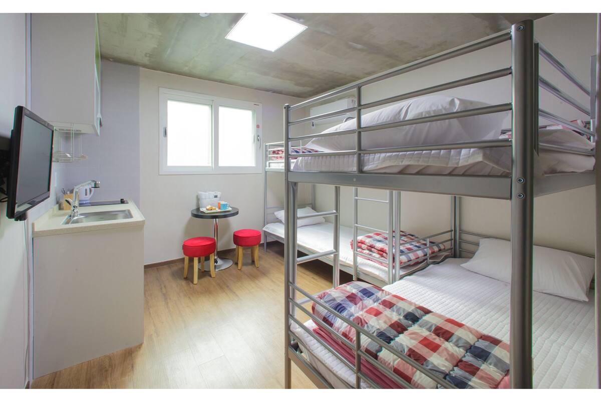 A bunk bed room with a sink, a small table, and two stools.