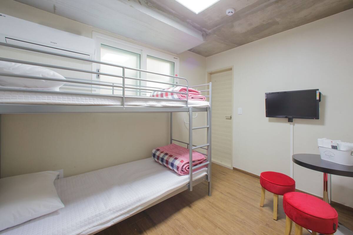 A bunk bed room with a TV, a small table, and two red stools.