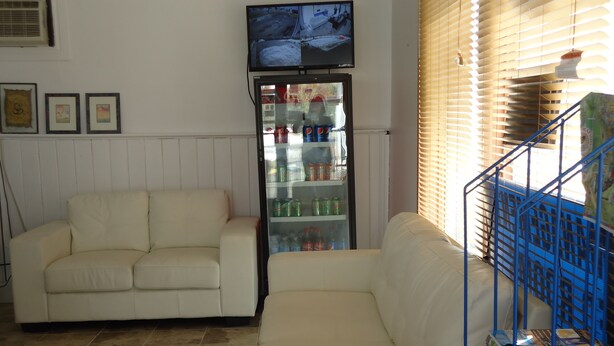 A living room with a white sofa, a television mounted on the wall, and a refrigerator stocked with beverages. - Star Inn by Elevate Rooms (Niagara Falls)