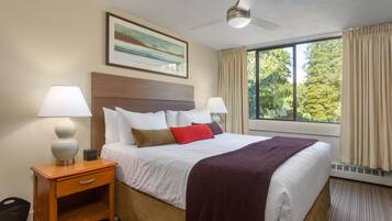 Une chambre d’hôtel avec un grand lit, deux lampes de chevet, une table de chevet, un ventilateur de plafond, une fenêtre avec des rideaux et un tableau encadré au mur.