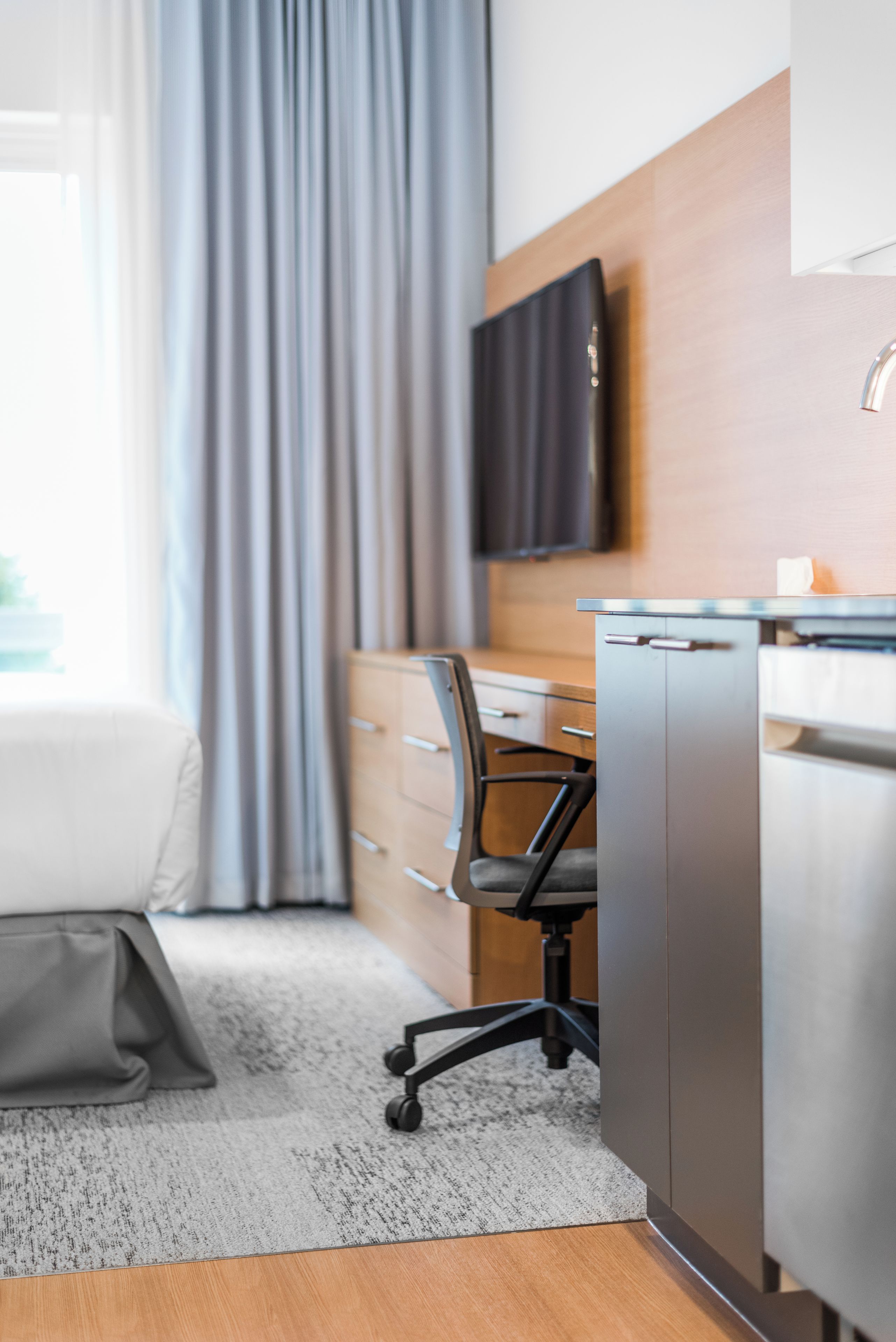 Quarto de hotel moderno com cama, escrivaninha, cadeira e televisão de tela plana na parede.