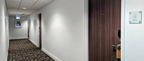 A hotel hallway with carpeted flooring, a wooden door, and a sign indicating room number 1013.