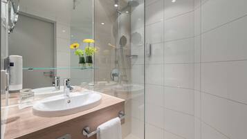 Un baño moderno con dos lavamanos, una cabina de ducha de vidrio y un espejo con un jarrón de flores amarillas.