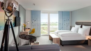 Habitació d'hotel amb un llit, escriptori, cadira i una finestra gran que dona a l'exterior.