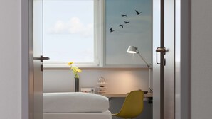Habitació d'hotel amb llit, escriptori, cadira, làmpada i finestra que mostra ocells.