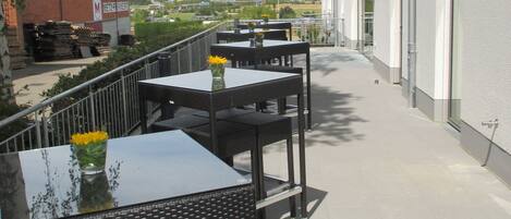 Un patio al aire libre con mesas y sillas, una vista despejada del paisaje urbano y un edificio con señalización al fondo.