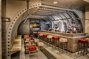 A bar area with a curved ceiling, bar stools, and a bartender preparing drinks.