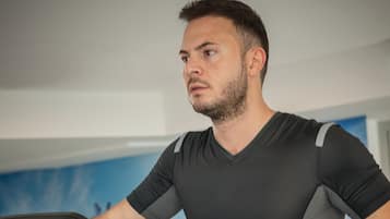 Eine Person trainiert auf einem Ellipsentrainer in einem Raum mit blauer Wand und Fenster.