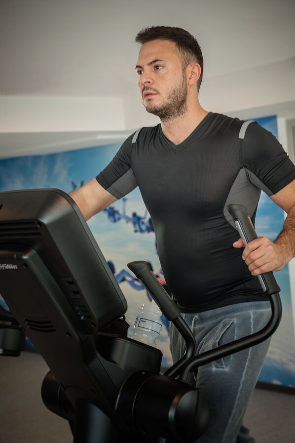 A person using an elliptical machine in a room with a blue wall and a window.