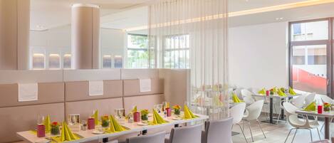 Un espace de restauration moderne dans un hôtel, avec de longues tables disposées pour accueillir plusieurs convives, des chaises aux couleurs neutres et un design épuré et minimaliste.