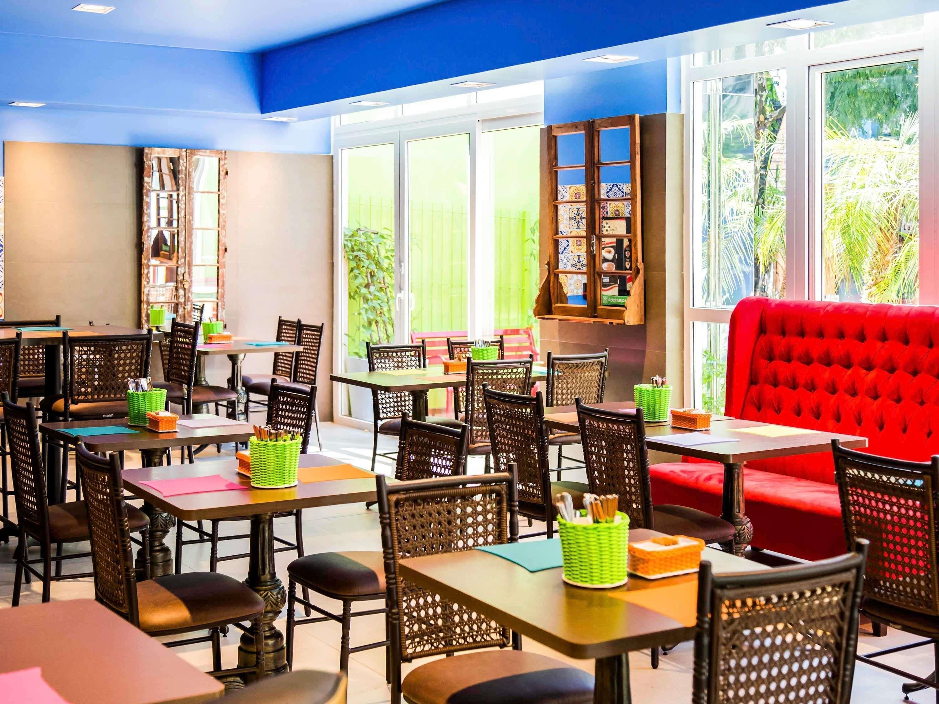 A restaurant with multiple tables and chairs, a red cushioned bench, and a wall-mounted shelf with decorative items.