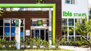 A modern hotel entrance with a green and white facade, a sign reading "ibis styles", and a visible entrance door.