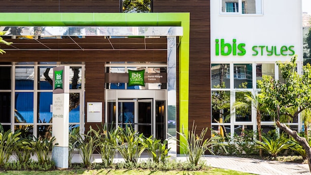 A modern hotel entrance with a green and white facade, a sign reading "ibis styles", and a visible entrance door.