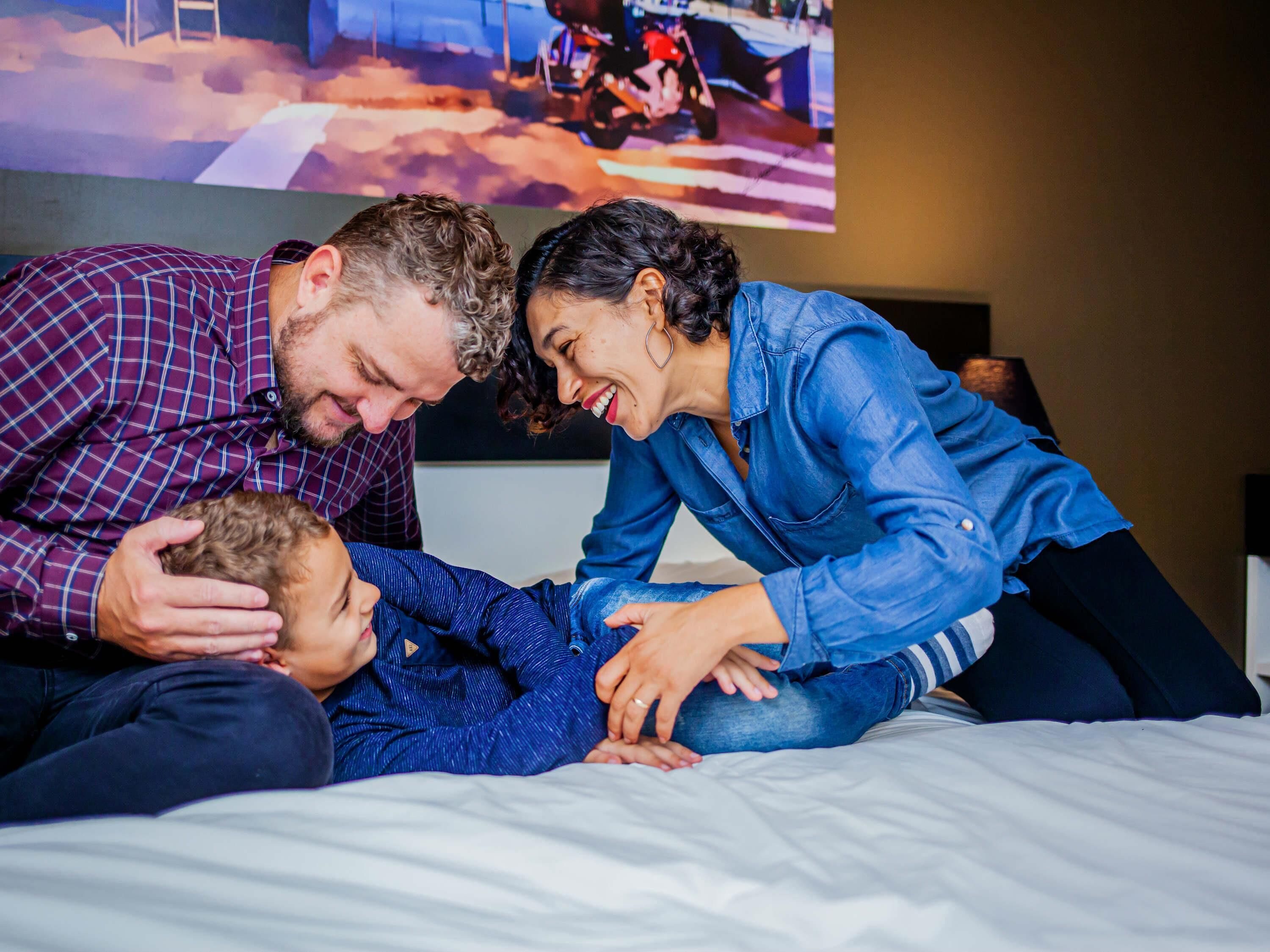 A family of three on a bed with a television in the background.