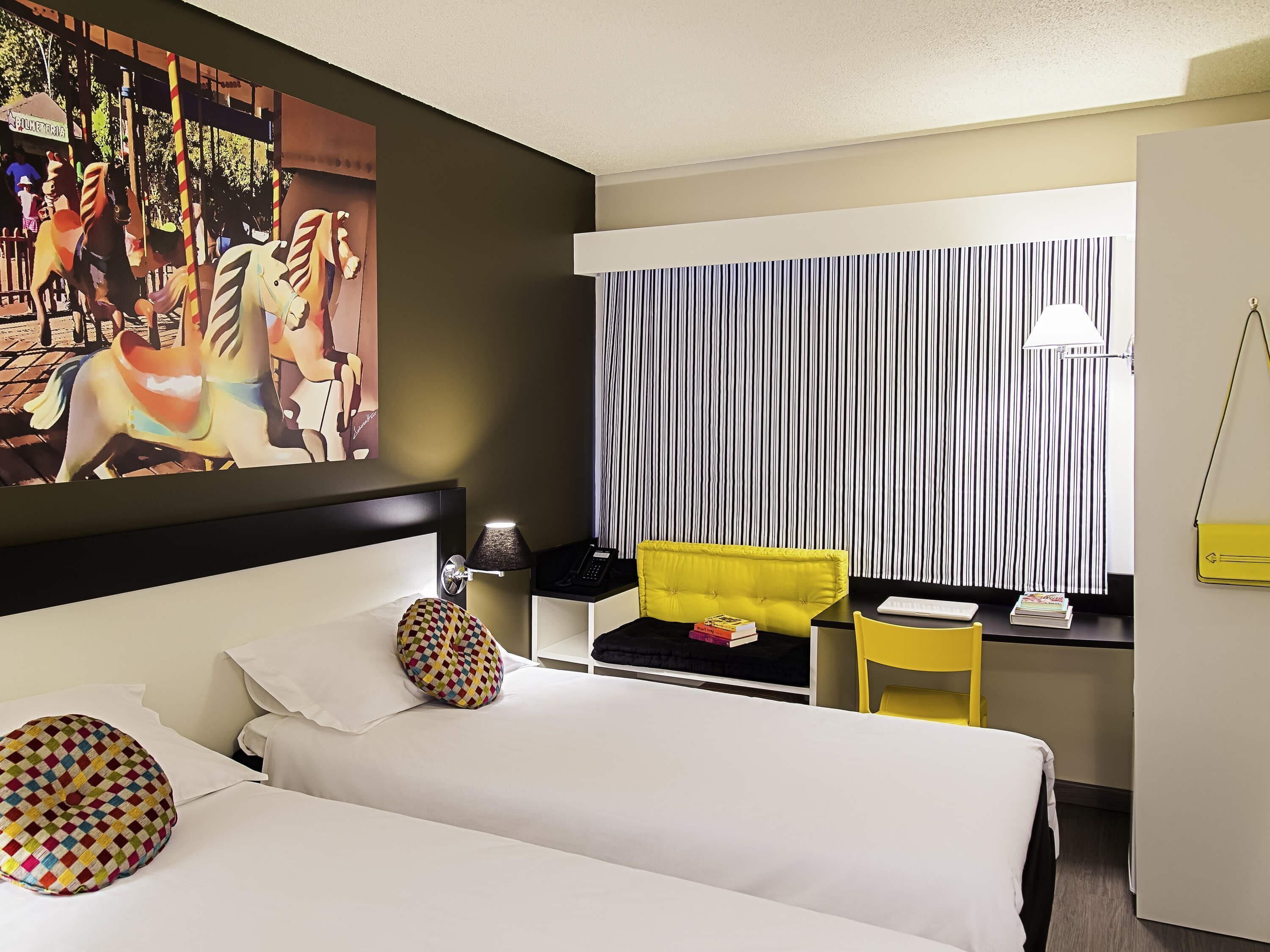 A hotel room with a bed, a desk with a chair, a lamp, and a striped curtain.