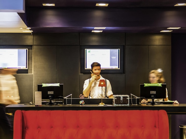 Un mostrador de recepción con un monitor de computadora, un teléfono y una pequeña mesa con una lámpara y un objeto decorativo.