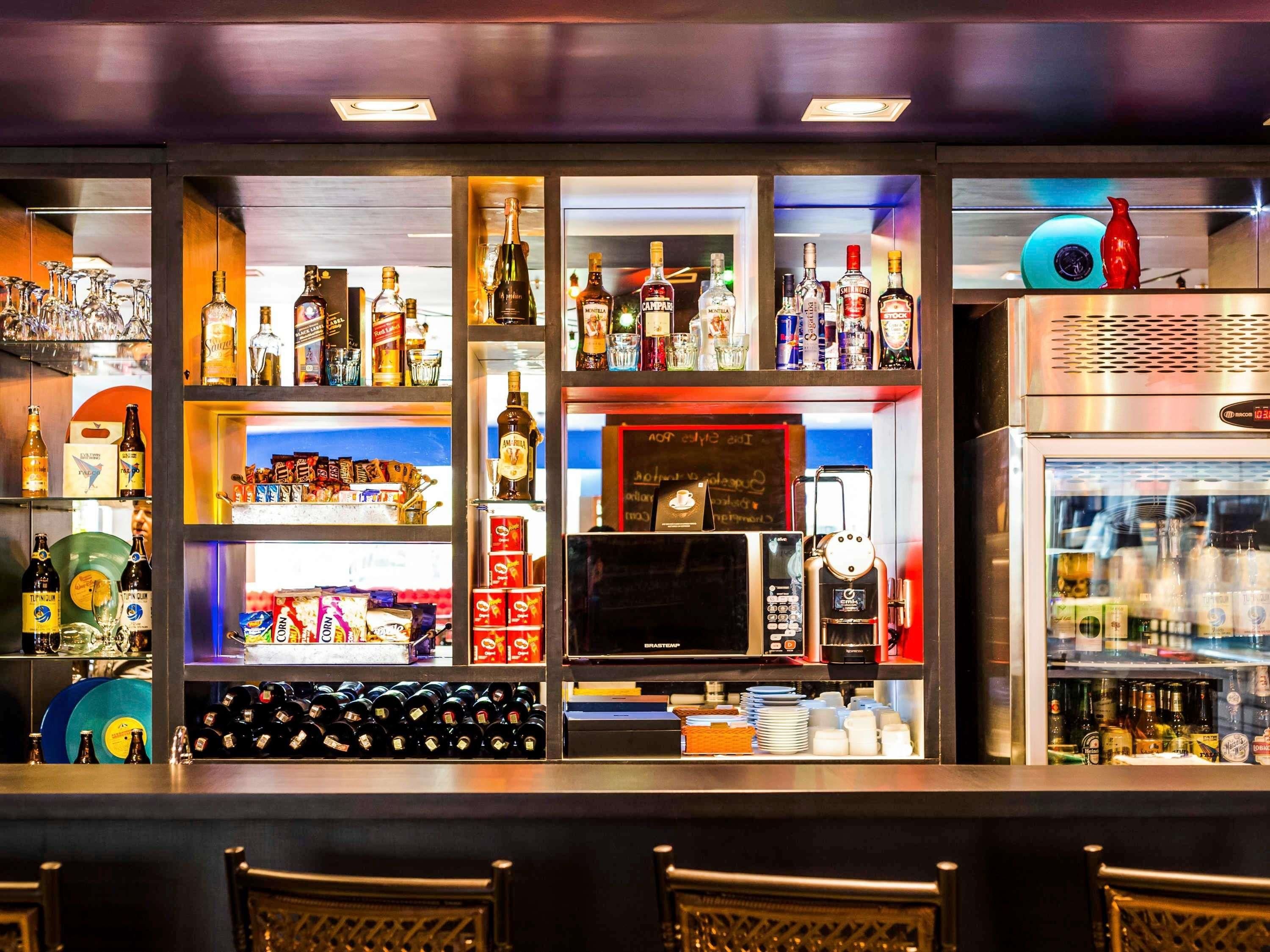 Uma área de bar com prateleiras de garrafas de bebidas, uma máquina de café e uma geladeira.