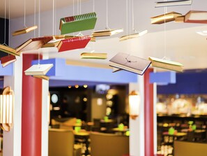 A modern interior with hanging bookshelves, red pillars, and a bar area in the background. - ibis Styles Porto Alegre Centro (Porto Alegre)